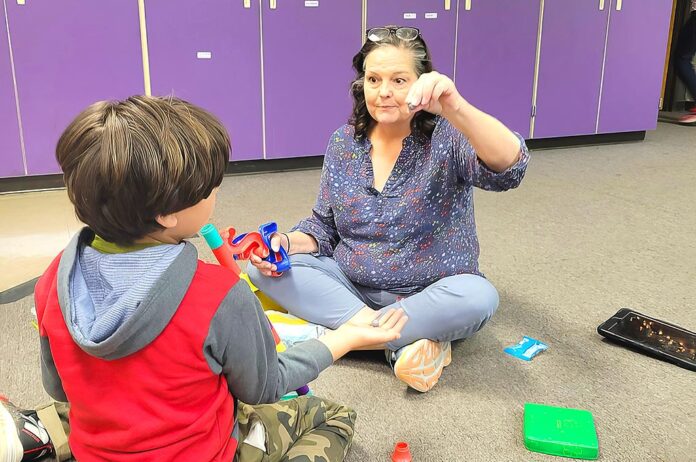 In this photo, Autism Specialist Val Valo uses play-based strategy to support the student’s social and language development. She encourage him to ask for the marbles in her hand as he builds a marble tower.