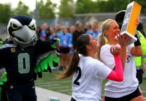 Tualatin seniors Isabella Hernandez (No. 2) and Ries Miadich receive the state title trophy from Blitz, mascot for the Seattle Seahawks.