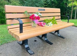 Joyce Stolze's memorial bench was unveiled on May 29, 2026. The plaque reads, "Joyce Stolze 1956-2024 Beloved Wife, Mama, Momo, & Friend"
