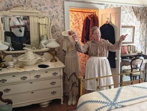 Dressed in period attire, docent Karen Hubachek describes the Middle Bedroom, which still features its original early-1900s English wallpaper from the Lloyd Wallpaper Distributor.