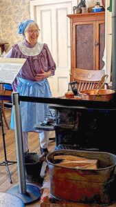 Docent Laura Baker in the Sweek House kitchen. The small cast iron wood stove and custom brick hearth were purchased by Althea Pratt-Broome and used for cooking and heating until just a few years ago. 