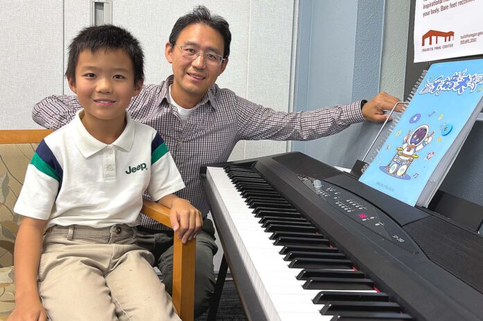 Andrew Gong and his father Patrick Gong both pose by the piano after Andrew Gong’s performance at the Juanita Pohl Center.